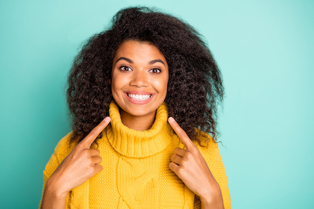 Closeup Photo Of Amazing Dark Skin Curly Lady Indicating Fingers On Perfect Teeth Advising Dentist Wear Yellow Knitted Pullover Isolated Blue Teal Color Background